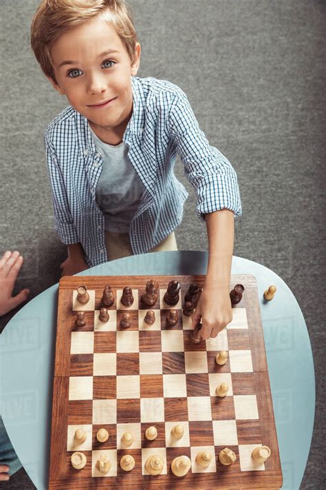 High Angle View Of Cute Little Boy Playing Chess And Smiling At Camera