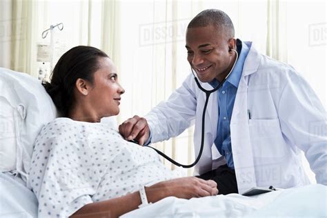 Male Doctor Checking Female Patient With Stethoscope Stock Photo