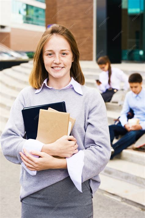 Premium Photo Ginger Schoolgirl Smiling Happily Standing With Textbooks Outside The School