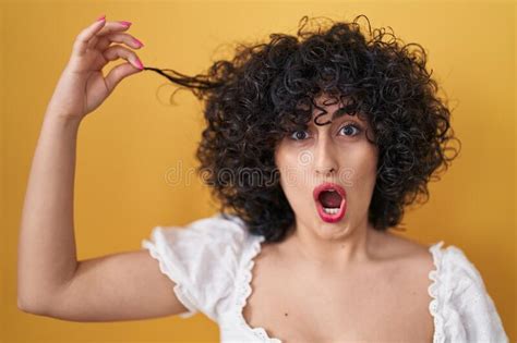 Young Brunette Woman With Curly Hair Holding Curl In Shock Face