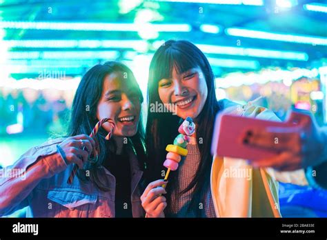 Happy Asian Girls Eating Candy Sweets And Taking Selfie At Amusement