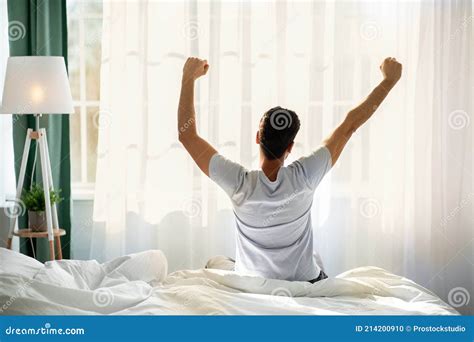 Good Morning Young Man Waking Up In Bed And Stretching His Arms