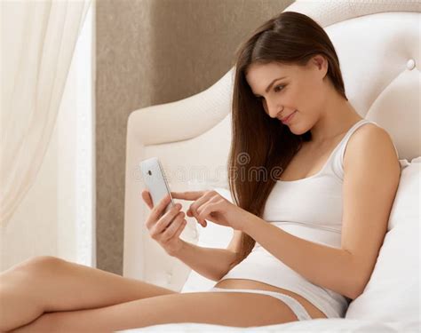 Portrait Of A Happy Woman Lying On Bed Using A Smart Phone Stock Image
