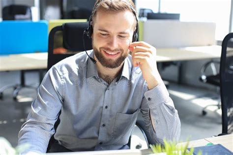 Smiling Male Call Center Operator With Headphones Sitting At Modern