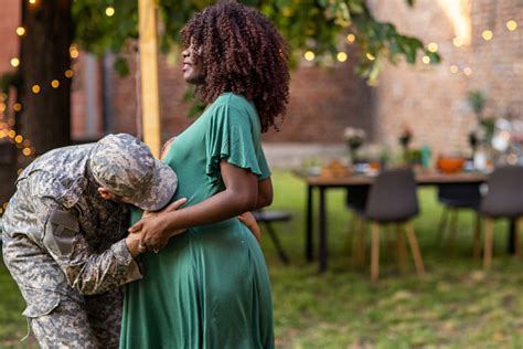 Soldier Kissing His Pregnant Wifes Stomach At A Back Yard Barbecue