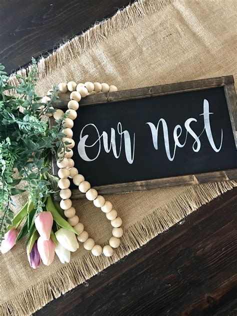 A Sign That Says Our Nest Next To Some Flowers On A Burlap Table Cloth