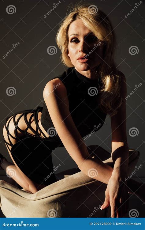 a blonde woman in a black dress sits in a chair in a dark room stock image image of dark