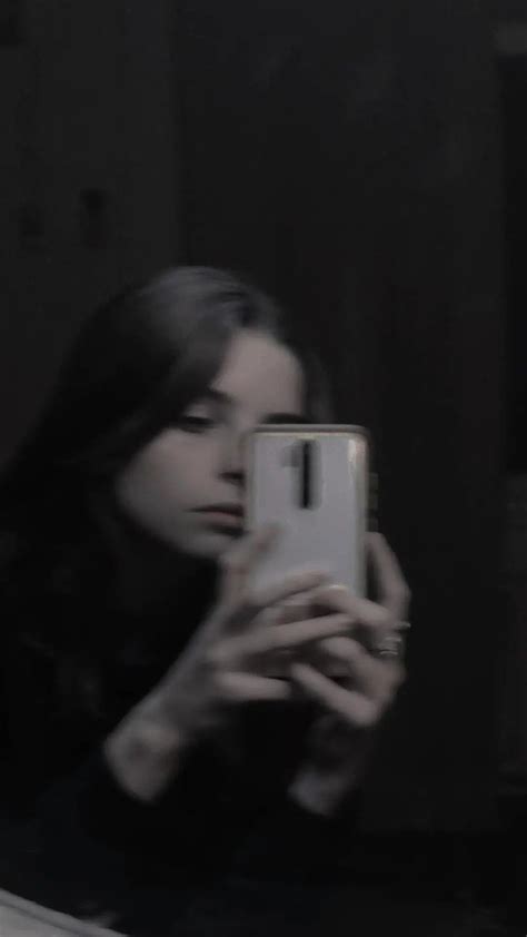A Woman Taking A Selfie In The Mirror With Her Cell Phone And Looking At It