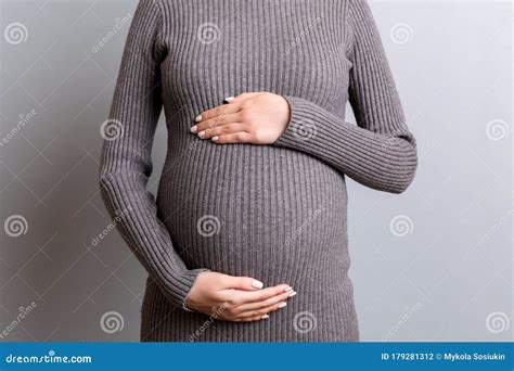 Cropped Image Of Pregnant Woman In Gray Dress Embracing Her Big Abdomen