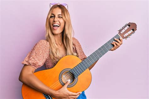 Beautiful Blonde Young Woman Playing Classical Guitar Winking Looking