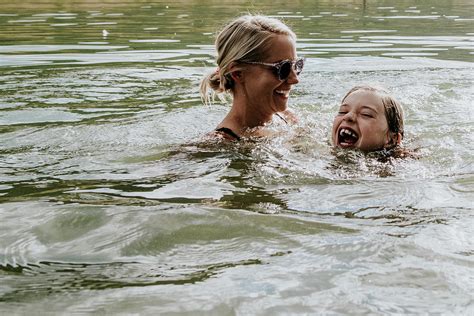 Mom And Young Daughter Joyfully Swimming In A Lake On A Sunny Day