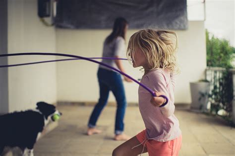 Side View Skipping Rope At Home With Mother Playing Tennis Against The