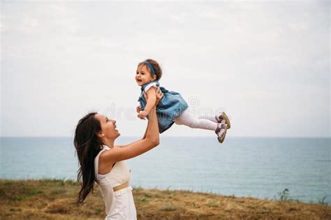 Happy Young Mother With A Small Daughter In Hands Hugging Near To The Lighthouse Outdoors