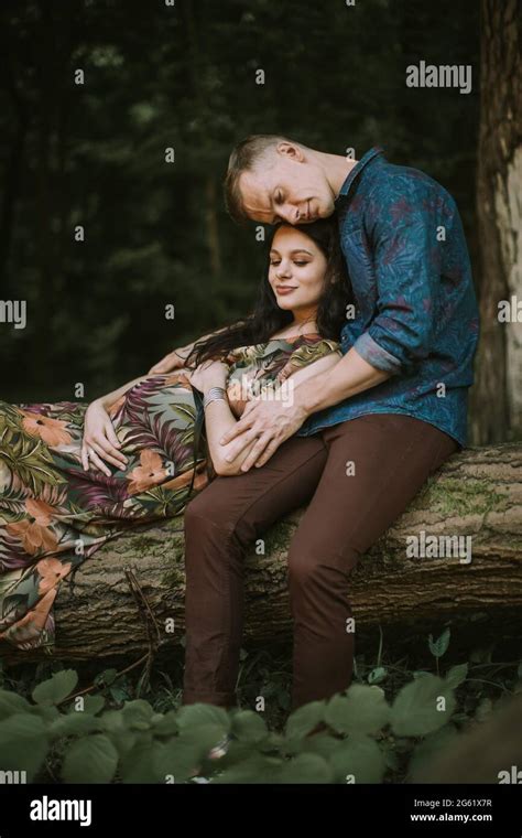 junge glückliche romantische schwanger paar sitzt auf dem gefallenen baum im wald küssen