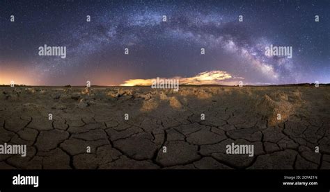 Dry Cracked Surface Of Ground And Colorful Night Starry Sky On Horizon