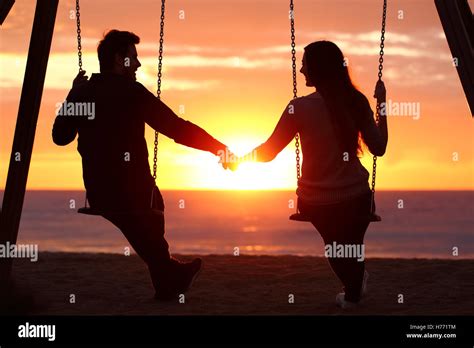 Back Light Portrait Of A Couple Silhouette Sitting On Swing Holding