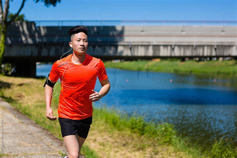 Young Chinese Man Running In The City Near A River By Stocksy
