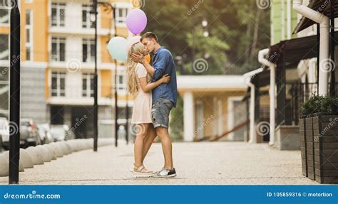 Passionate Young Couple Kissing In Street Holding Colorful Air