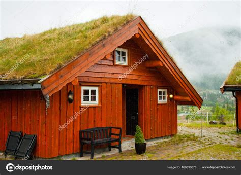 Traditional Norwegian Wooden House Standing On A Lawn And Mountains In
