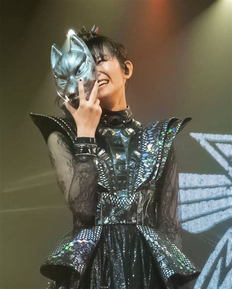 A Woman In A Black And Silver Dress On Stage With Her Hand Up To Her Face