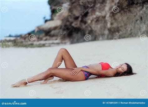 Slender Tanned Woman In Colored Swimsuit Posing On Beach With White