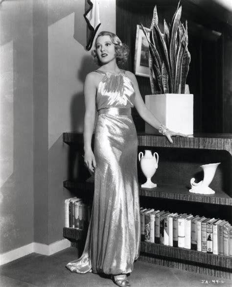 A Woman In A Long Dress Standing Next To A Shelf With Vases On It