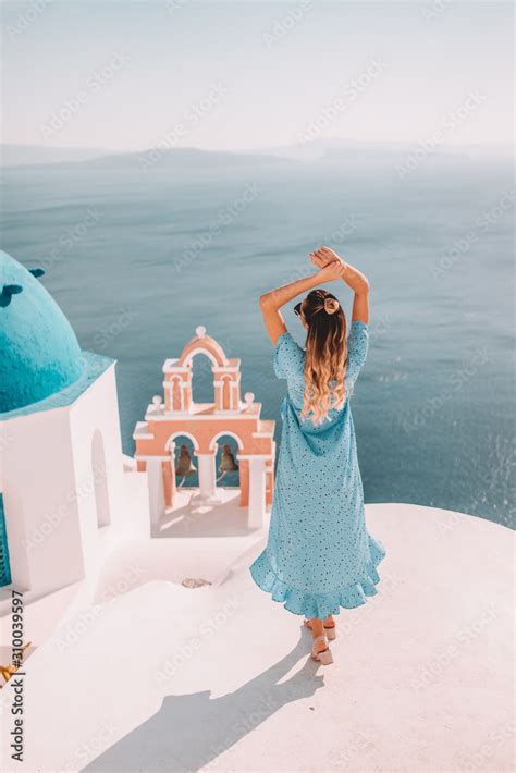 Young Woman With Blonde Hair And Blue Dress In Oia Santorini Greece