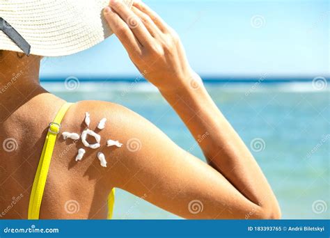 Back View Of Young Woman Tanning At The Beach With Sunscreen Cream In Sun Shape On Her Shoulder