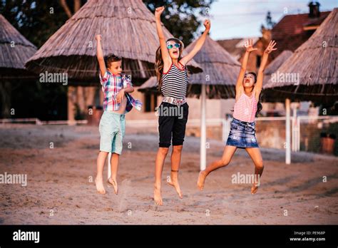 Portrait Of Happy Children Having Fun While Jumping On The Sandy Beach