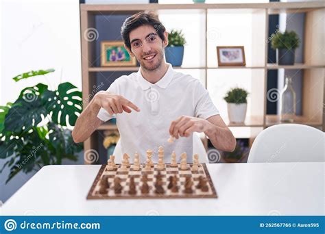 Young Hispanic Man Playing Chess Sitting On The Table Smiling Happy