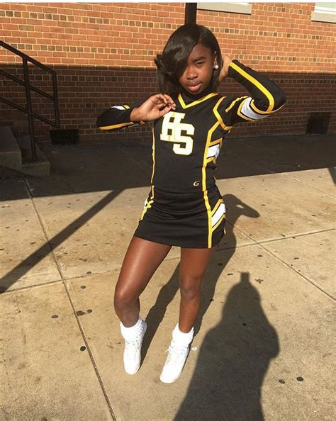 A Woman In A Cheerleader Uniform Posing On The Sidewalk With Her Hands Behind Her Head