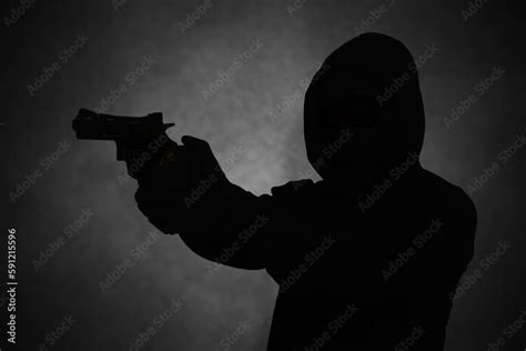 mysterious man wearing black hoodie holding a pistol shooting with a gun silhouette and dark