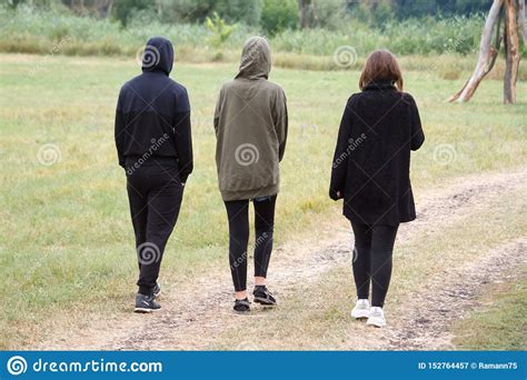 Rear View Of Three People Walking Along A Dirt Road In A Field Early In