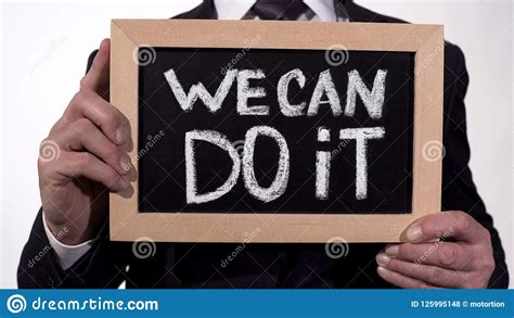 We Can Do It Motivation Phrase On Blackboard In Businessman Hands