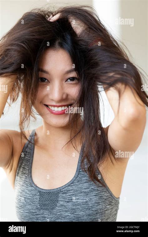 Young Beautiful Asian Girl Smiles And Plays With Her Hair She Is Wearing A Sporty Top And Red