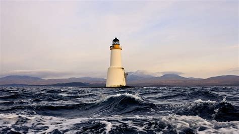 Lighthouse In Rough Seas Sea Lighthouse Waves Clouds Mountains Hd