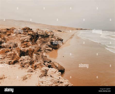 A Stormy Sea Waving Near A Sandy Shore Surrounded By Rocks Stock Photo