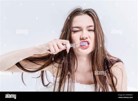 Sleepy Brunette Woman Brushes Her Teeth While Sitting On The Bed In The