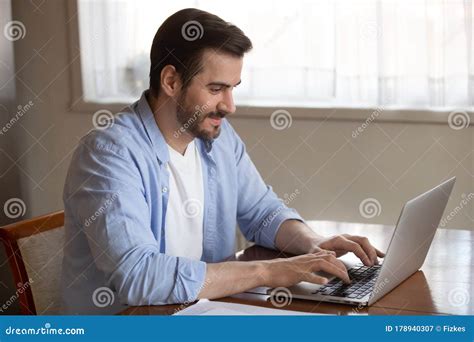 Handsome Pleasant Young Man Working Remotely On Computer At Home Stock