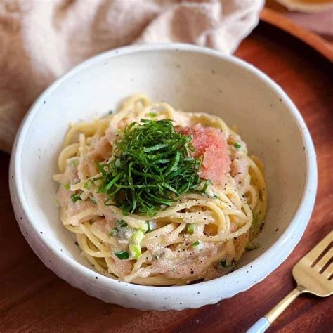 a white bowl filled with pasta on top of a wooden table next to a fork