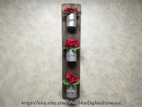 Three Metal Canisters With Red Flowers In Them Are Hanging On A Wooden Wall