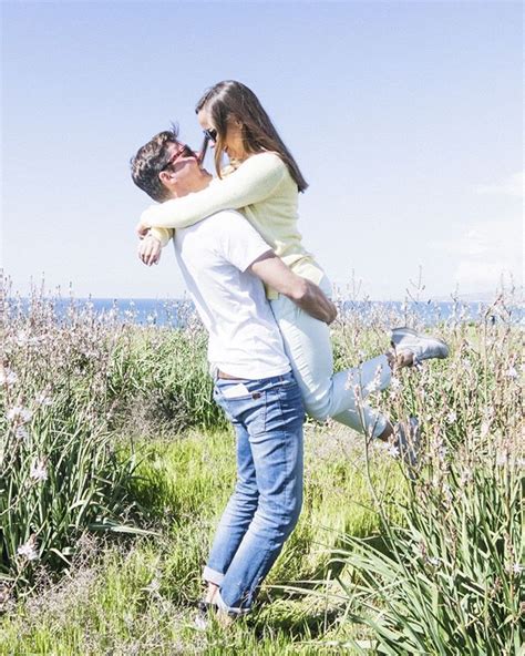 A Man Holding A Woman In His Arms While Walking Through Tall Grass Near The Ocean