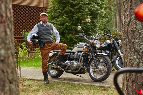 A Man Standing Next To A Parked Motorcycle In The Grass With Trees