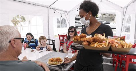 RACE COUNTS - Young Waitress Serving Food to Customers in Outdoor Tent Wearing a Mask