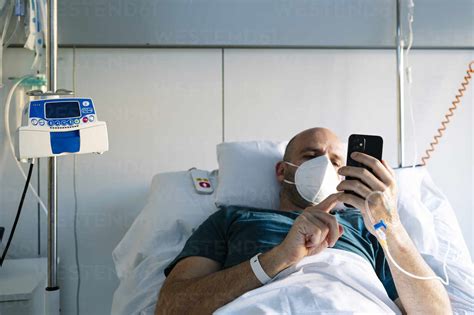 Patient With Iv Drip Using Mobile Phone While Lying On Bed In Hospital