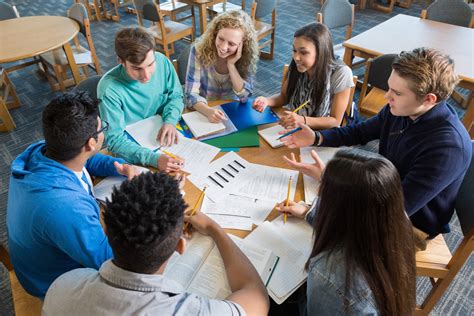 Large Diverse Group Of Students Studying Together In Library Teacher