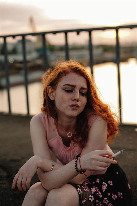 Young Redhead Woman Smoking Cigarette While Sitting On Bridge In City Photograph By Cavan Images