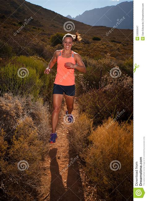 Blonde Female Trail Runner Running Through A Mountain Landscape Stock