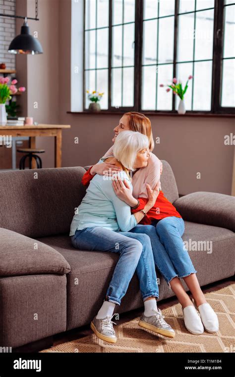 Elderly Granny Having A Hug With Attractive Granddaughter On Sofa Stock