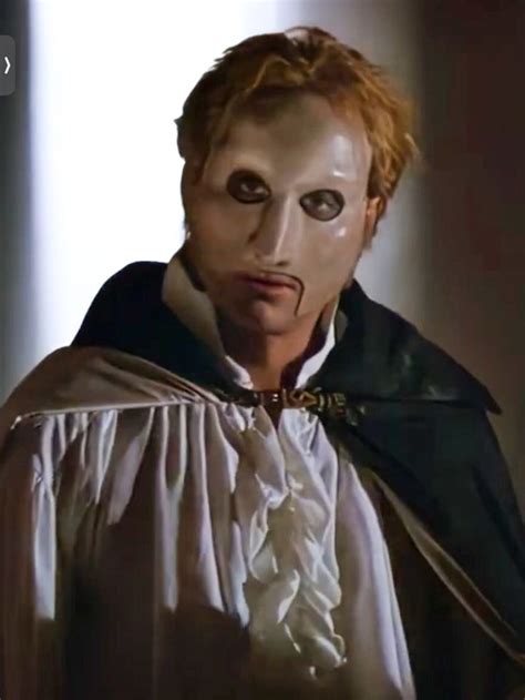 a man with red hair wearing a white mask and black cape is looking at the camera